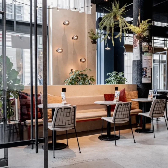 Sitting area at Anne&Max coffee bar in Tilburg with wall lights, hanging plants, and a garden room atmosphere – hospitality interior by Studio JAAF.